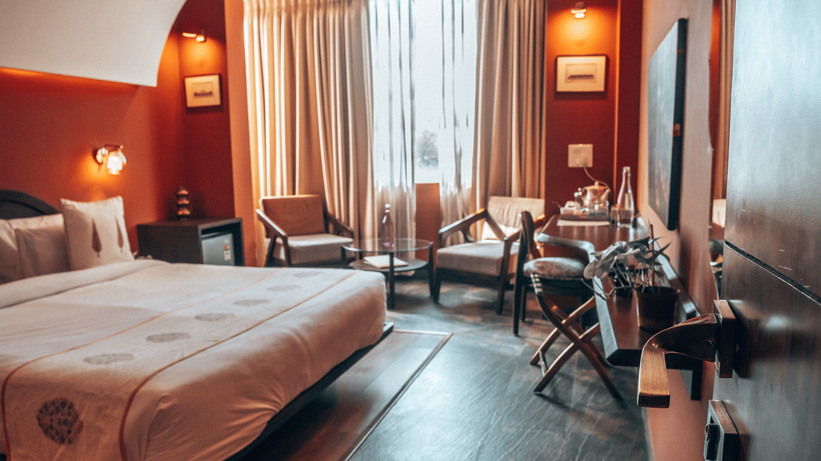 Spacious guest bedroom featuring a king size bed, elegant warm wall decor, large windows, and a comfortable seating area.