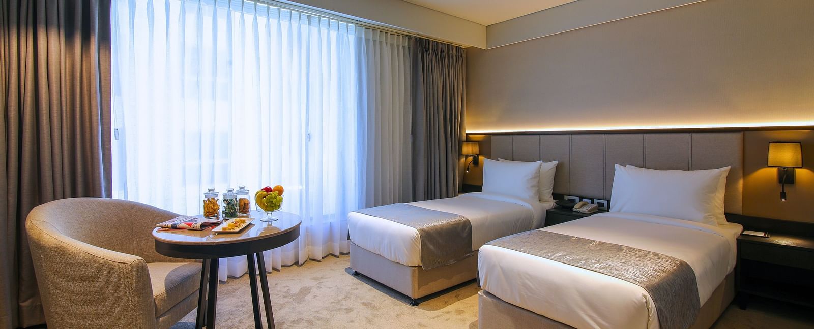 Twin beds with a chair and table in front of it inside one of the rooms - Essentia Premiere, Pune