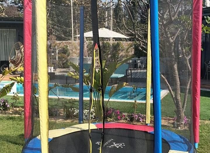 A trampoline with a safety net placed on a well-maintained green lawn under the open sky.