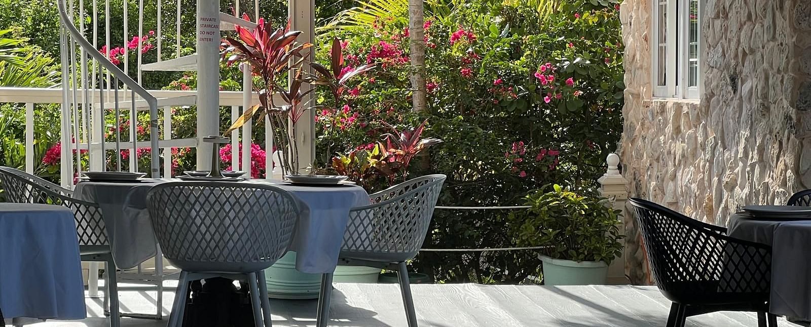 Outdoor dining area with black chairs and spiral staircase surrounded by lush plants | A Stone's Throw Away