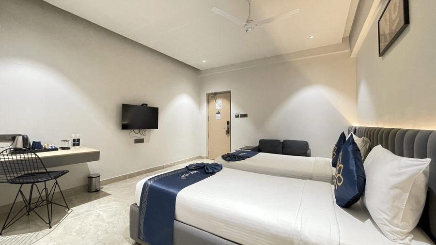 A hotel room at Hotel Kyzen HiTech City featuring a king bed with blue accent runner a work desk wall-mounted TV grey headboard and light tiled flooring in a modern setting.