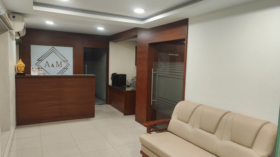 A lounge area featuring a dark wooden desk with a decorative centrepiece and a light-coloured sofa | A & M Rooms and Residences