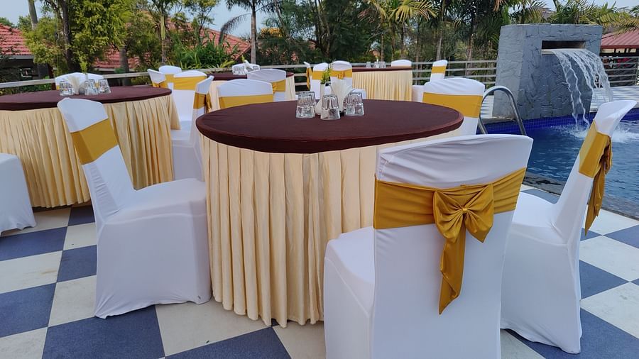 Outdoor event space with round tables and white chair covers | Open Deck | Woodstock Resorts, Coorg