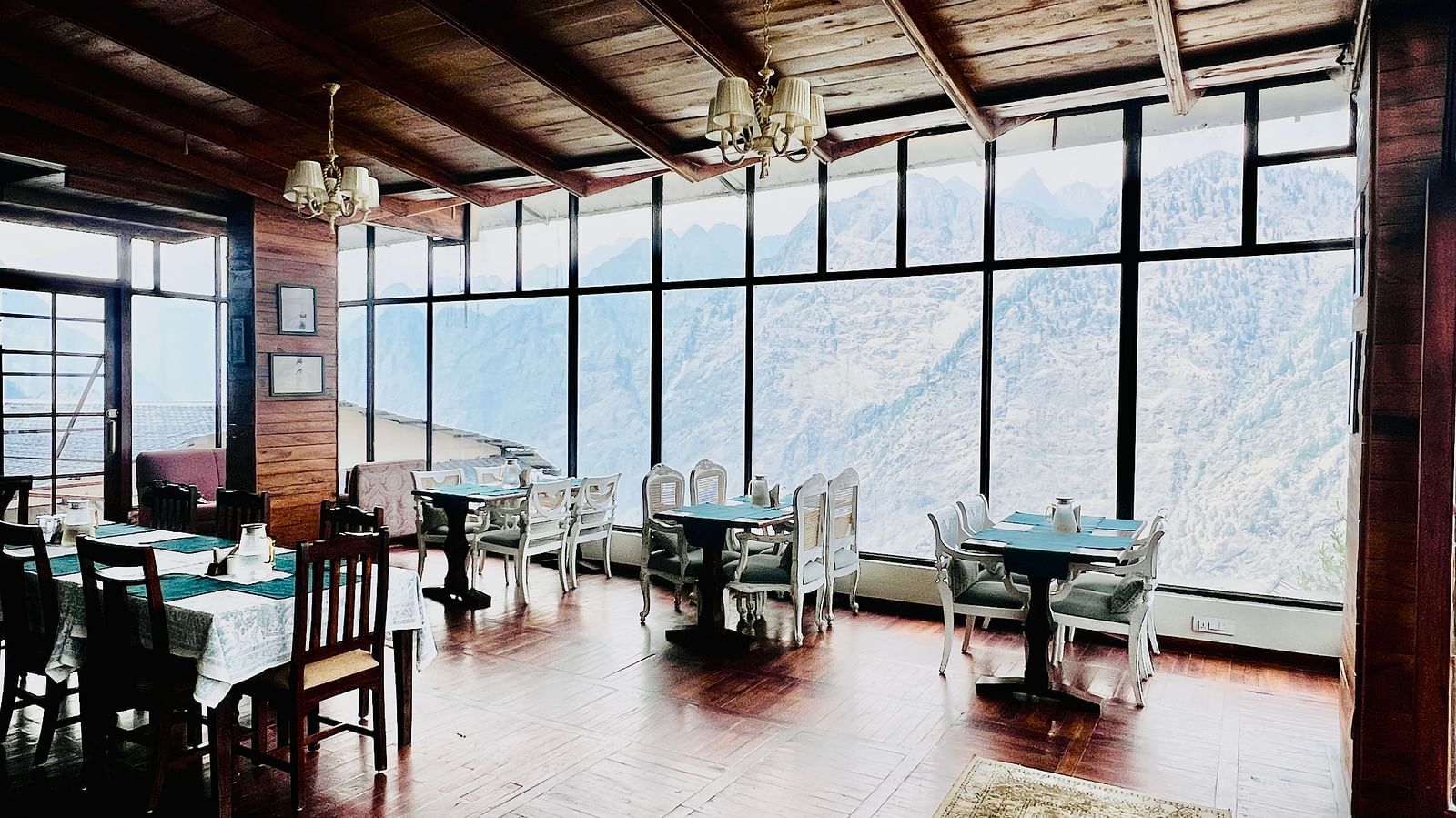 Wood-paneled dining room with large windows offering panoramic views of the mountains  | Faraway Cottages, Auli