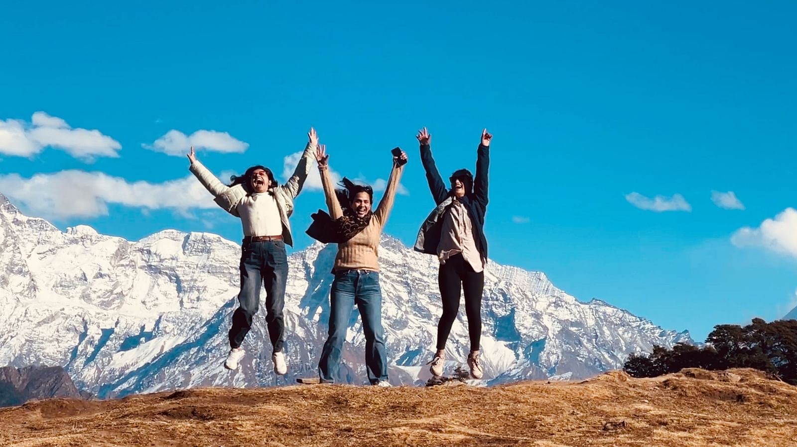 Three people jumping and posing for a photo at Gorson Meadow  | Faraway Cottages, Auli