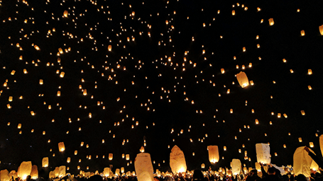 A group of people releasing sky lanterns into the night sky with many lanterns floating into the sky. Lanterns are usually flown during the New Year in Chennai.