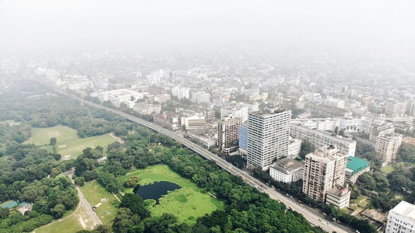 A bird's-eye view of Kolkata with greenery on one side and buildings on the other separated by a road.