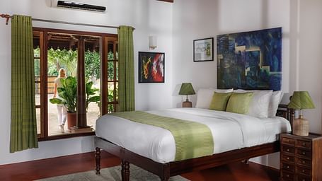 A room with a bed, wooden decorative items, and a glass window overlooking the view - BluSalzz Villas - Muhamma Resort, Alleppey