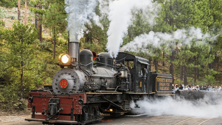 Steam locomotive with wheels emitting smoke while stationary on tracks near a station