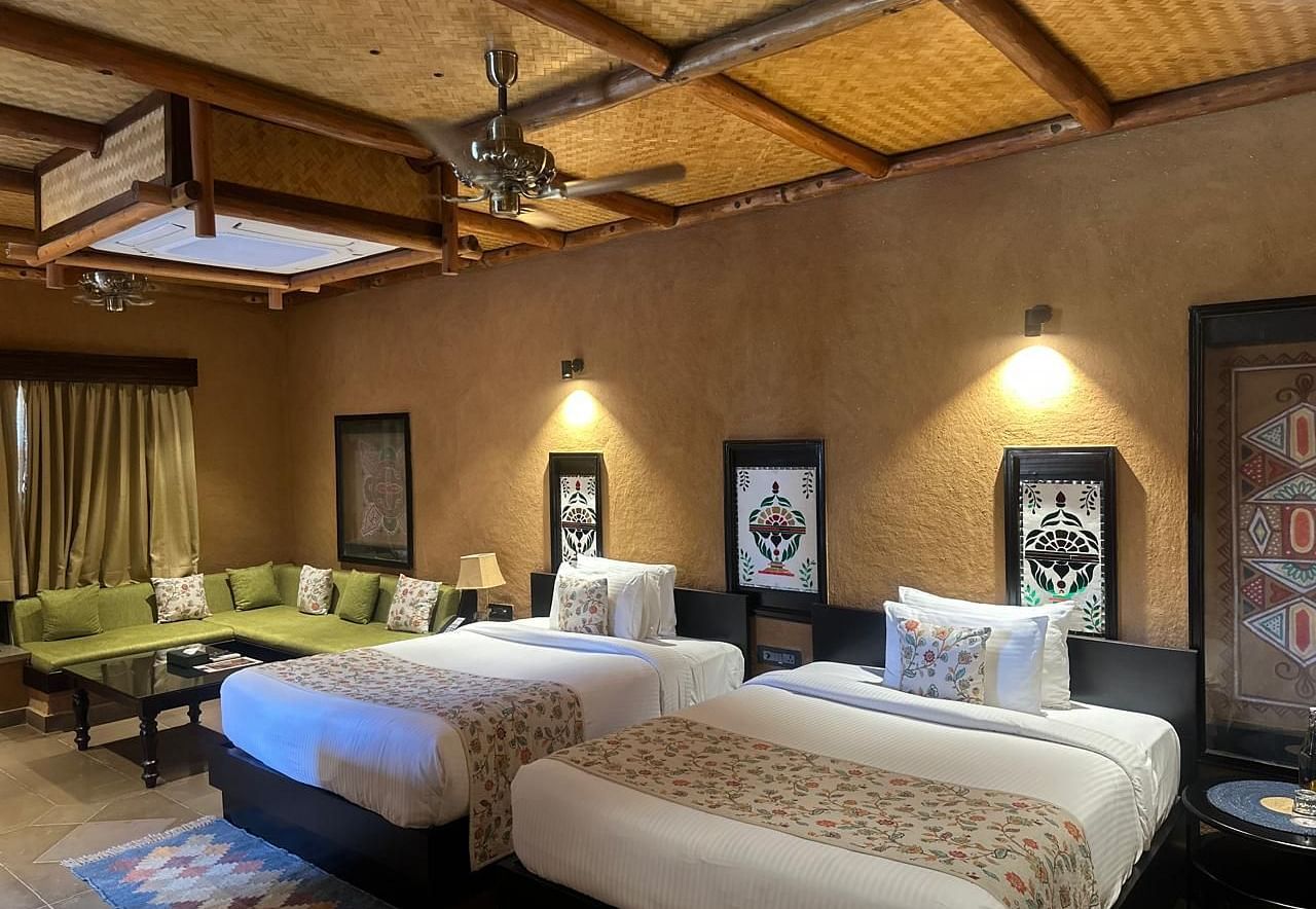 A well-appointed suite bedroom with two beds and a comfortable sofa area at Aamaghati Wildlife Resort.