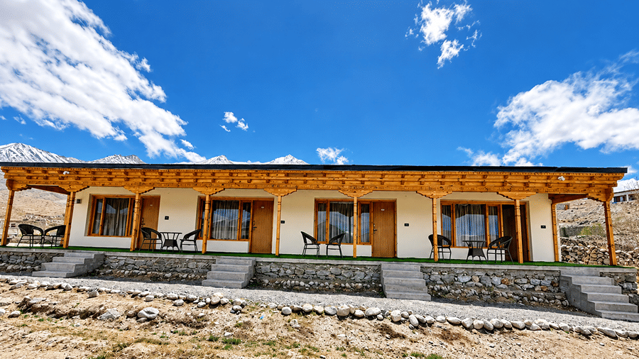 Facade of Royal Rebo Pangong with wooden balconies and large windows beneath a bright blue sky.