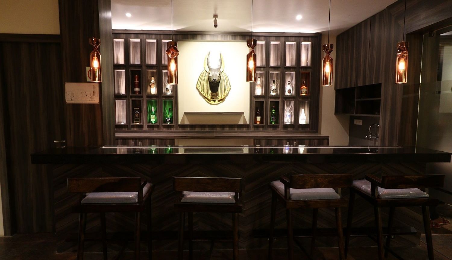 A dimly lit, sophisticated bar area with a long counter, bar stools, and bottles displayed on shelves - Sea Hills Hotels, Sri Vijayapuram (Port Blair)
