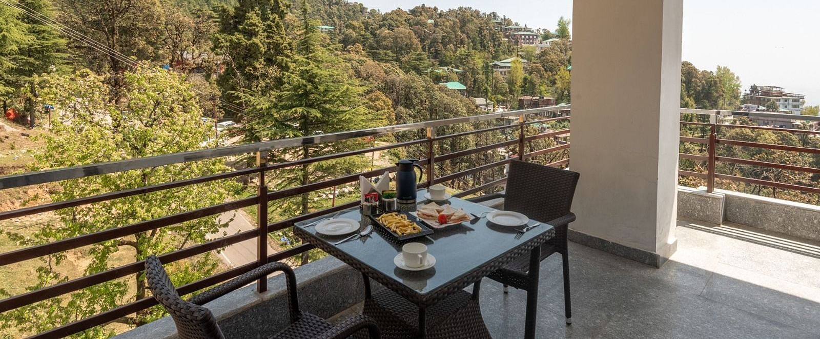 Balcony of Family Suite features an intimate seating table for two, spacious area and a view of the lush green hills and landscapes on a sunny day at DLS Hotel Shiva Sanctuary & Spa, Dharamshala.