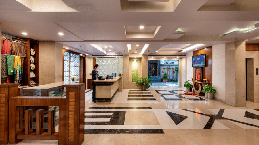 lobby at Libra Lords Inn Jaipur featuring a well-lit modern interiors with marble floor, wall mounted TV, a reception desk, and a boutique display with traditional clothes and jewellery