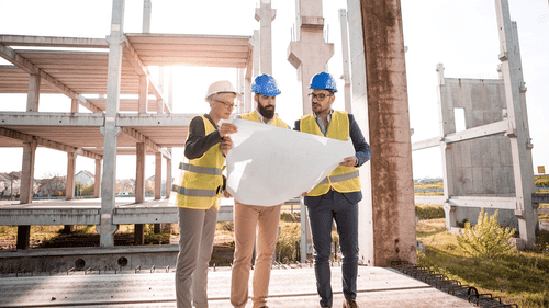 Three architects discussing a plan and holding a chart with an under-construction building in the background.
