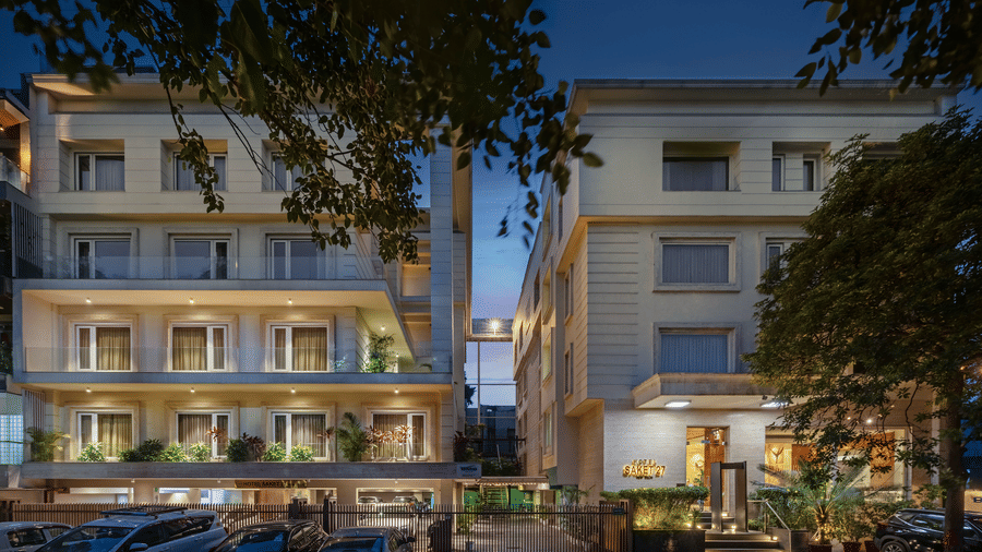 Night view of Hotel Saket 27’s exterior showcasing a multi-story building with balconies, illuminated façade, a grand entrance, and an inviting ambience for visitors.