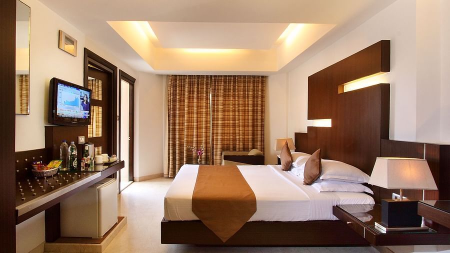 A side view of Studio Room with comfy bed and TV with side bed lamp at The President Hotel Jayanagar, Bangalore 