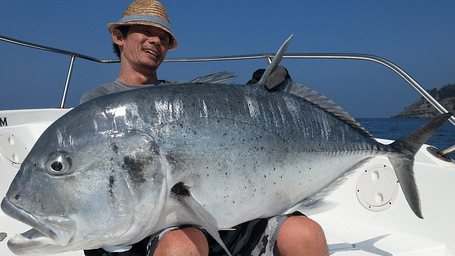 A man sitting on a boat, holding a large fish resting on his thighs.