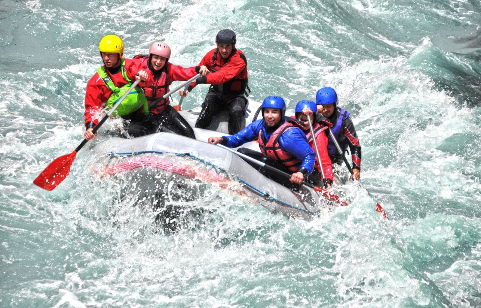 A group of people rafting on a single raft in a rushing river, splashing water around them. 