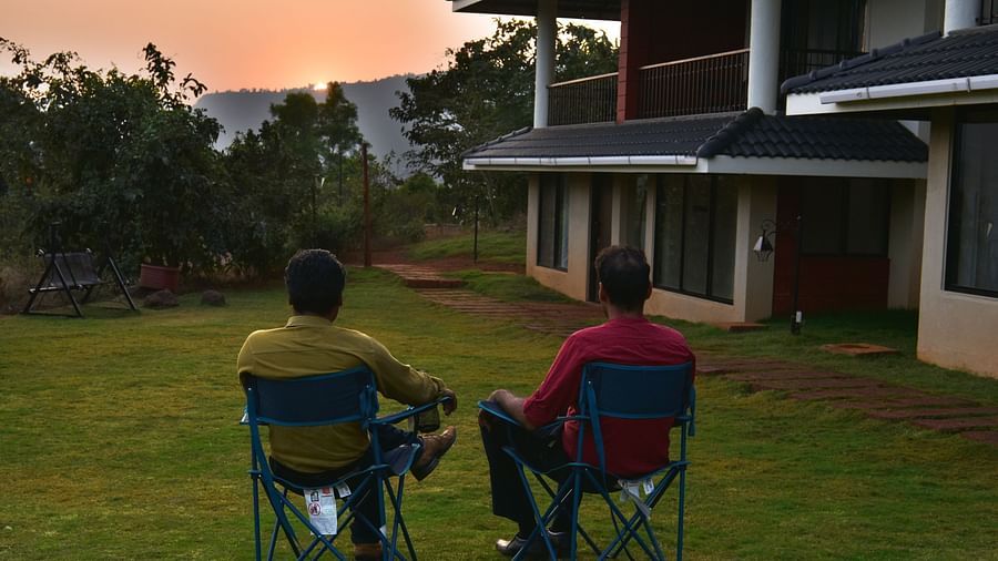 Relaxing outdoors at Forest Escapes Koyna, two people sit in chairs facing the resort buildings.