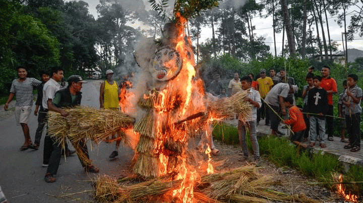 A crowd gathered on a street watching the ritual burning of a straw effigy representing a demon during the Ghantakarna festival in Nepal.