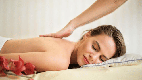 a woman lying on her stomach with her eyes closed and getting massage on her back with a flower next to her