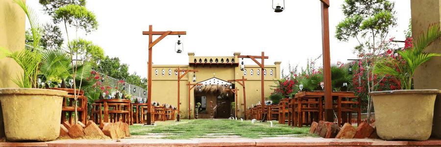 Outdoor walkway at Themis Mudhouse Resorts featuring rustic wooden lamp posts, potted plants, and a village-style mud entry archway.