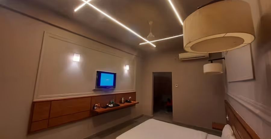 A sleek and modern hotel room featuring warm LED strip lighting, a TV, and a stylish bed- Max Hotel Prayagraj.