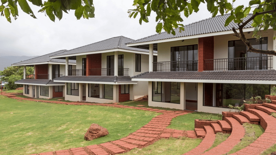 Exterior view of Agreen Hotels with a modern resort facade, red brick pathways, manicured lawn, and lush greenery under an overcast sky.