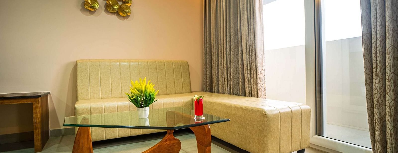 A bright seating area at Mansha Palace includes a modern glass table, a comfortable sofa, and balcony access.