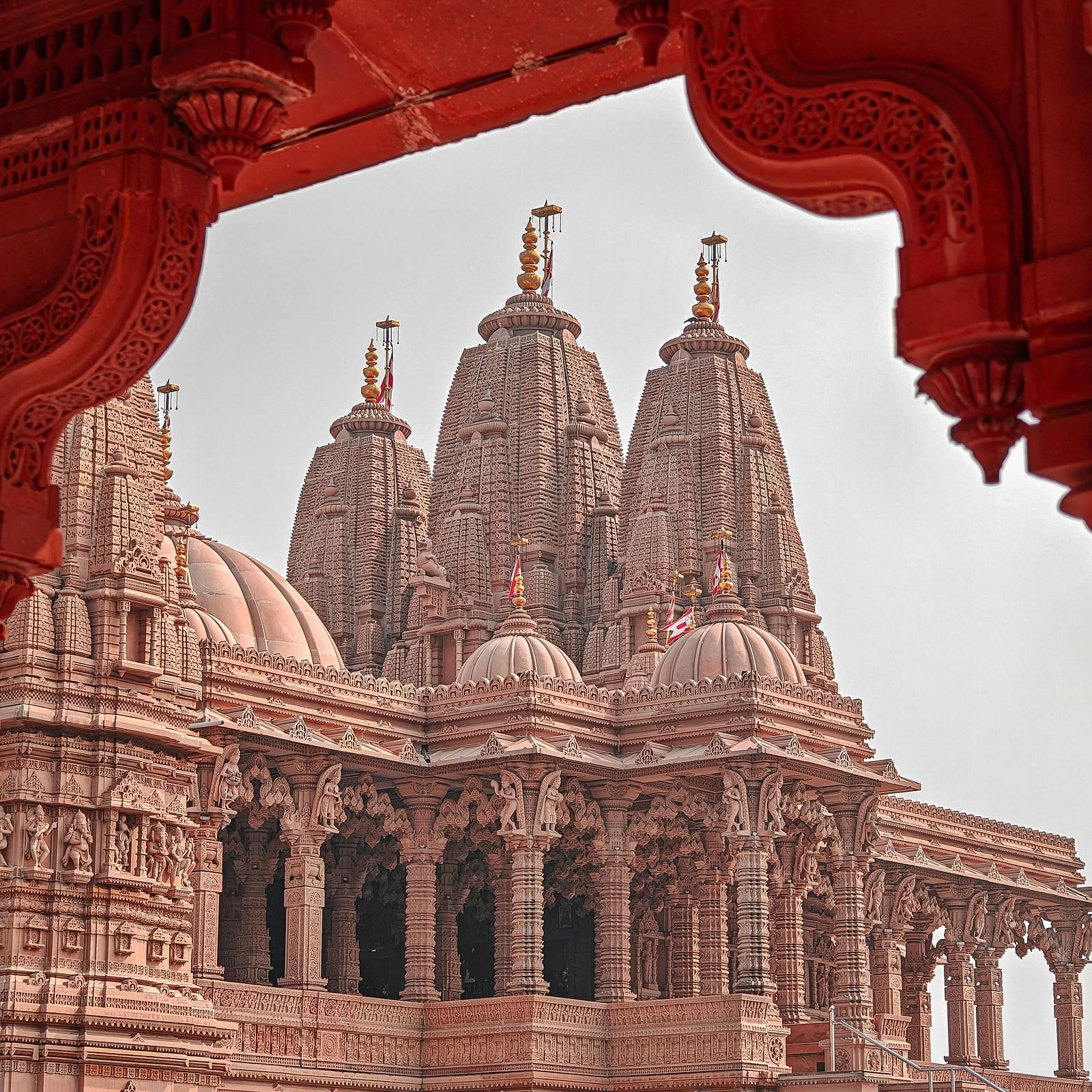 A detailed, light brown stone temple with multiple spires and domes is framed by a red, ornate archway.