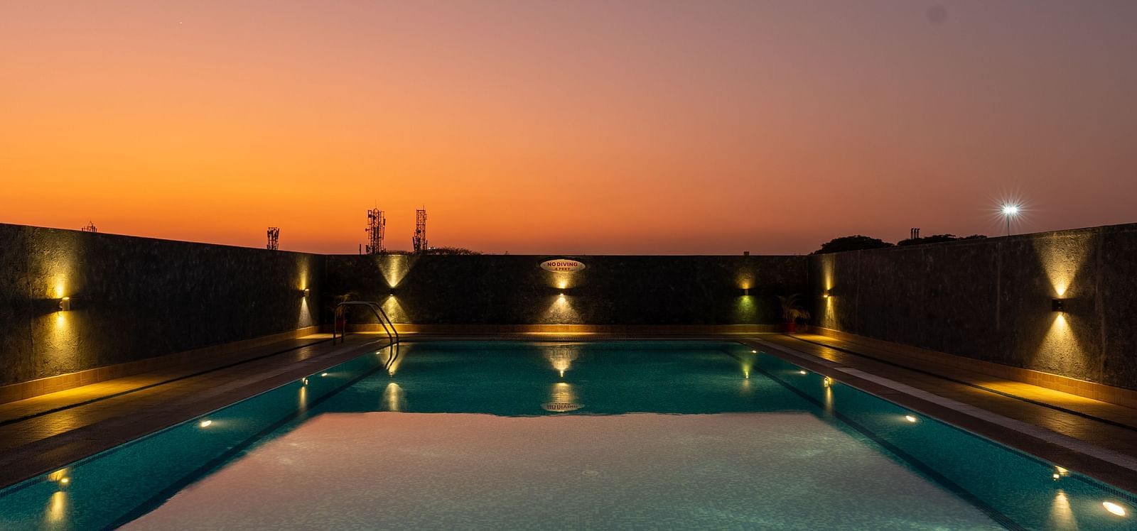 An image of an outdoor swimming pool installed with dim lights on the sides of it - Hotel Pai Vista, Mysore