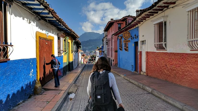 A person walking on a stone paved road with buildings on each side and a mountain in the background