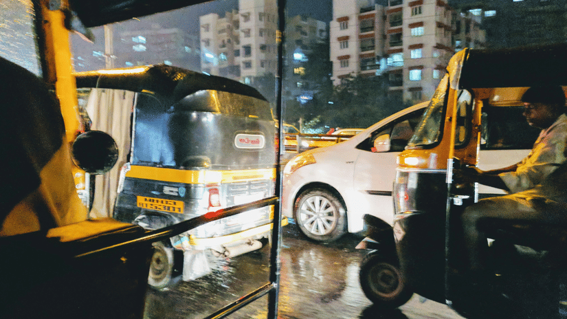 View from an auto-rickshaw moving through busy city traffic at night with vehicles and illuminated streets