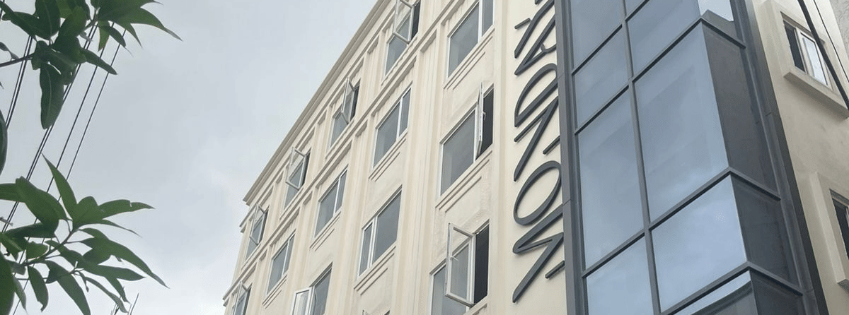  Contemporary exterior view of Monday Premium, Madhapur, showing a multi-storey building with a glass-fronted stairwell and a cream-coloured facade. 