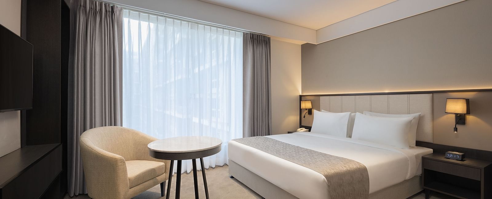 Deluxe King Room with a king size bed and a comfortable chair beside a large window at Essentia Premiere, Pune. 