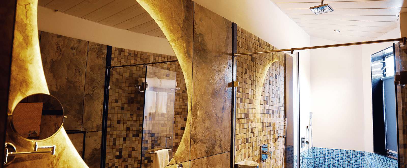 A modern bathroom of Luxury Villa with Sitout boasting a large, uniquely shaped mirror with warm lighting and contemporary fixtures at The Qualia Resort Club & Brewery, Udaipur.