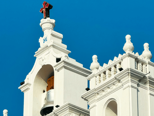 A close-up shot of the facade of a church with a white exterior featuring a shiny bell at the top.