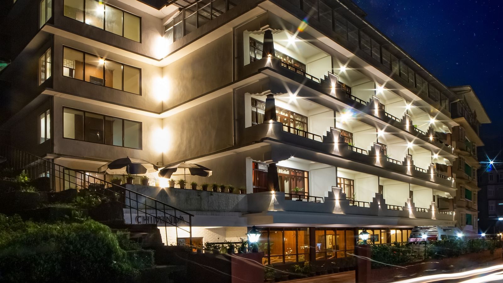 The illuminated facade of Sumitel, Pelling, at night, showcasing its contemporary design with streaks of light from traffic.