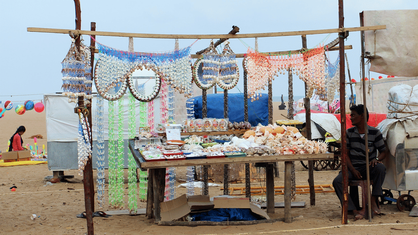 a street market on the beach with a person sitting next to a stand