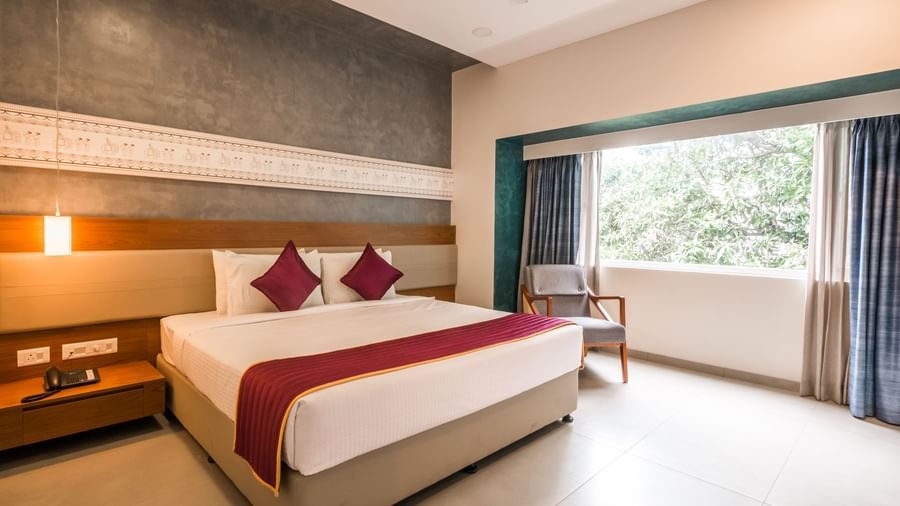 A bright hotel room with a large bed and ample natural light, providing a relaxing ambience at Shilton Dee Cee.
