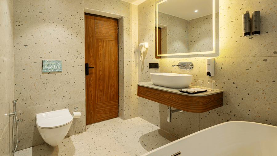 A bathroom featuring a big mirror, a wash basin on a counter with toiletries, soap dispensers and a hair dryer on a wall, and a closed door | Summit by the Ganges Beach Resort & Spa, Rishikesh