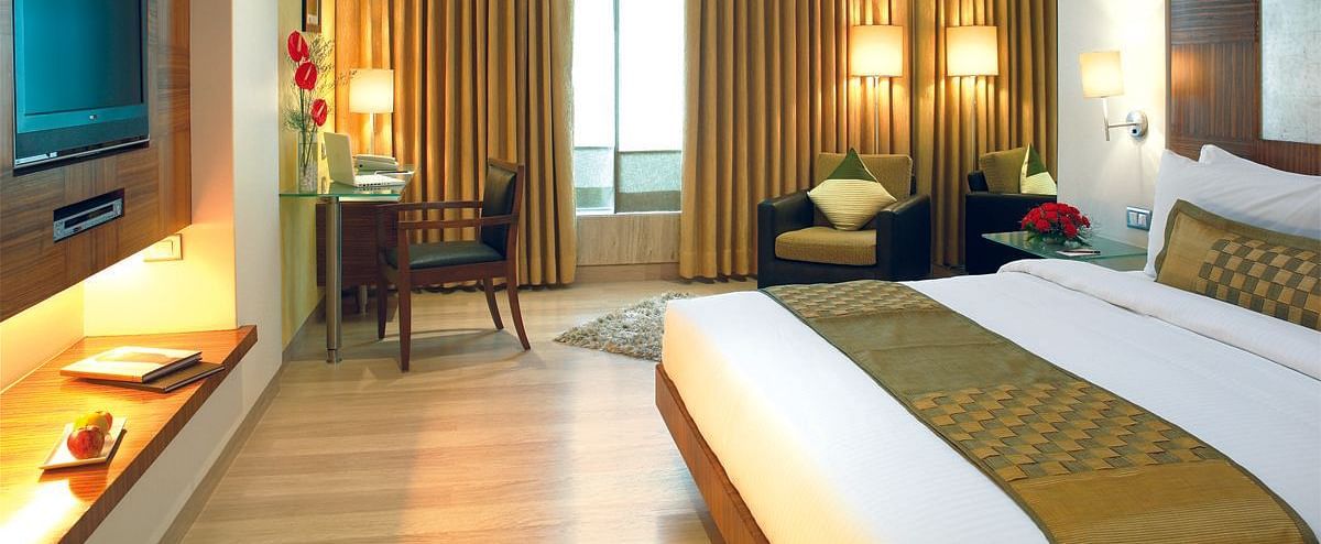 Image of a the executive room featuring a king size bed, a study table and chair, flat screen television, and an expansive window with golden curtains. | Mirage Hotel