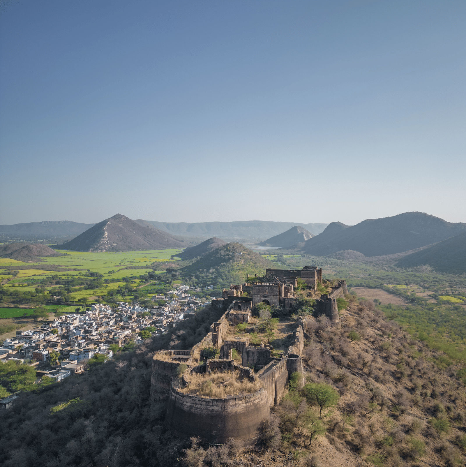 Aerial view of a historic hill fort surrounded by green valleys and distant mountains – Utsav Camp Sariska