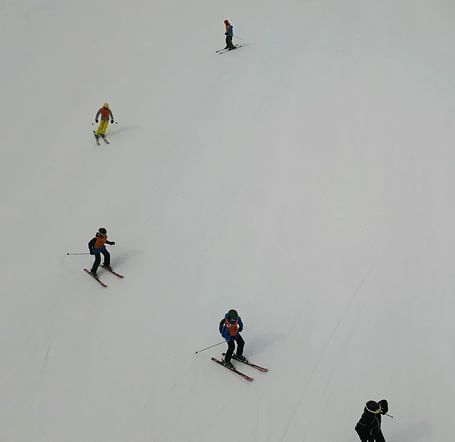 Skiers scattered across a snowy slope, seen from above.