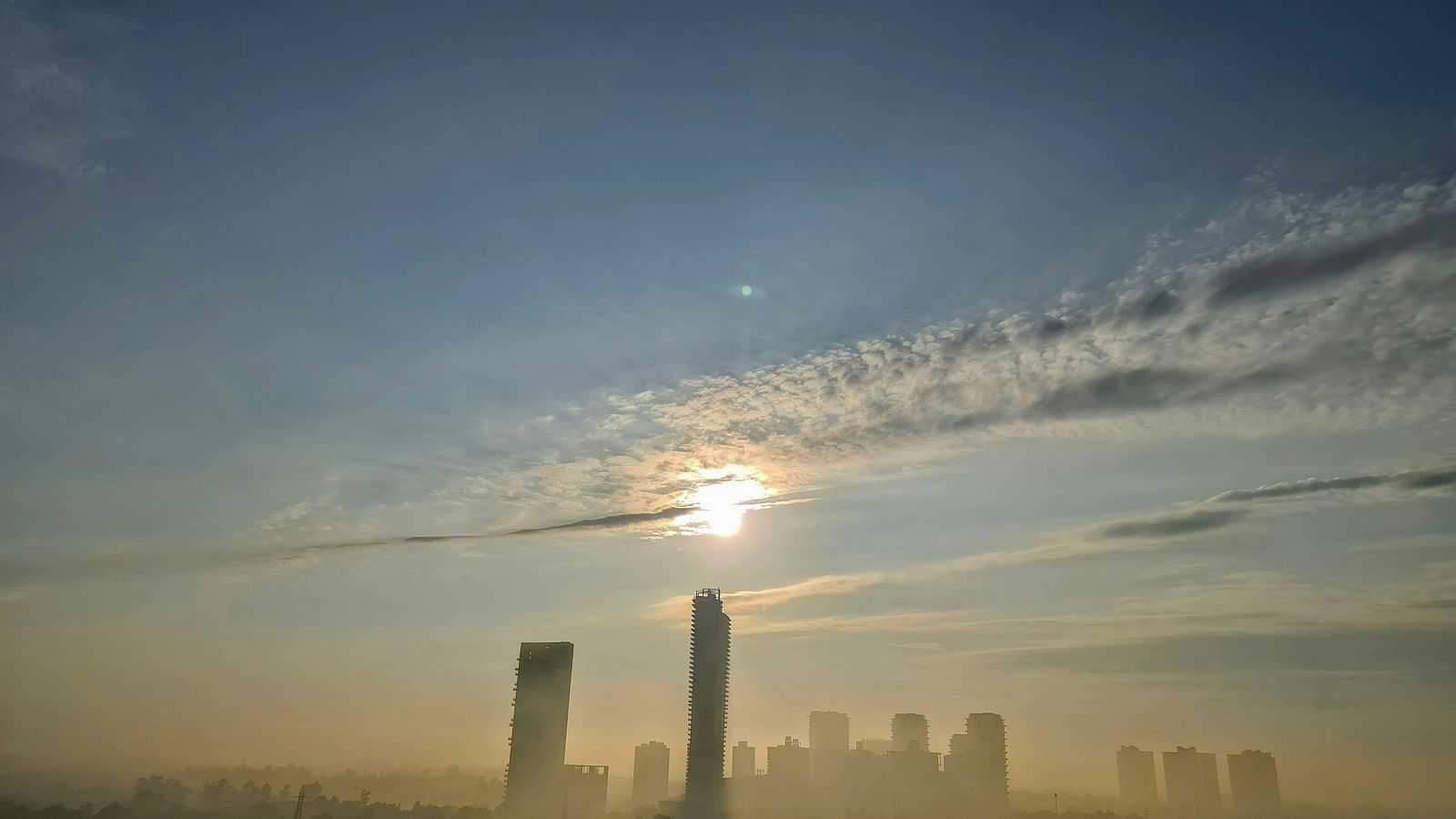 An overview of the city of Gurgaon with the sun just above a high rise building.