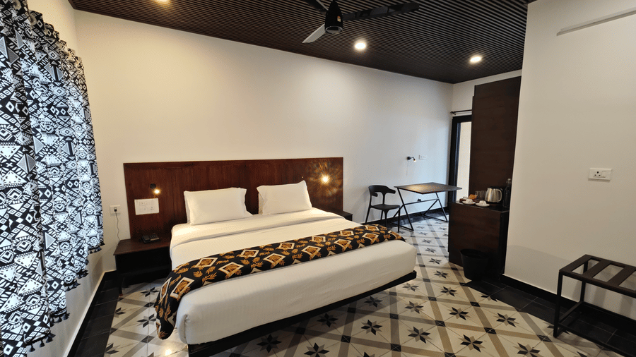 Modern guest room interior with a king size bed, decorative floor tiles, and dark wood ceiling accents - Ibex Resorts, Malampuzha (Kava Eco Camp and Caravan Park)