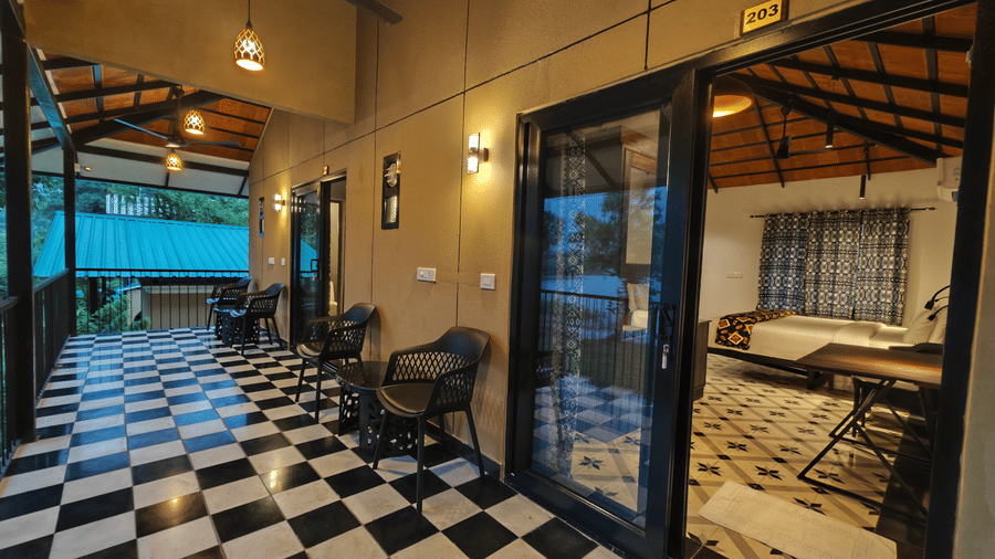 Exterior corridor with checker tiles leading to glass-door to guest rooms under a warm-lit canopy - Ibex Resorts, Malampuzha (Kava Eco Camp and Caravan Park)