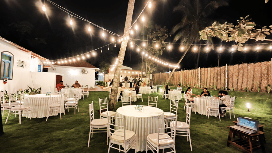 Outdoor night event setting with white chairs, a projector screen, and decorative string lights over a lawn at Ibex Resorts, Coimbatore (Kakarla).