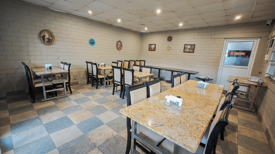 Spacious dining area at Ibex Resorts Valparai Mistly featuring neatly arranged wooden tables and chairs on a checkered floor with soft natural lighting and a cosy atmosphere perfect for group meals and family gatherings.